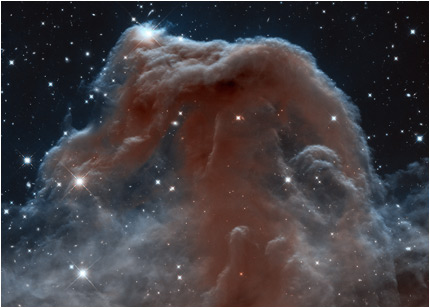Looking like an apparition rising from whitecaps of interstellar foam, the iconic Horsehead Nebula is shown in infrared light as imaged by the Hubble Space Telescope. The heart of the nebula appears in red like a capital letter T with wilted edges. Wrapped around this heart are white, gray, and transparent-looking clouds of material. All on a start-studded background. 