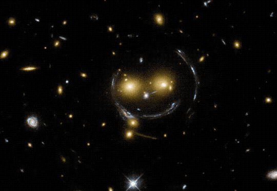 This slideshow of images from the Hubble Space Telescope starts with an image of galaxy cluster SDSS J1038+4849, which looks like it has a smiley face. There are two bright orange “eyes,” a white blob for a nose, and the “smile” is formed by arcs caused by gravitational lensing. The second, fourth, and fifth images show Abell 370, Abell 2218, and SDSS J1004+4112, which are galaxy clusters. Sprinkled throughout are galaxies that appear smeared or stretched due to a phenomenon called gravitational lensing. This effect can help scientists map the presence of dark matter in the universe. The third image shows extreme gravitational lensing of LRG 3-757. In the image there is a glowing orange blob that is a luminous red galaxy. Surrounding the galaxy is the image of an even-more distant galaxy which has been distorted into a nearly complete circle.