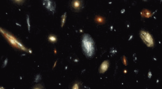 This animated GIF illustrates how a gravitational lens would distort our view or background galaxies. The animation opens with an image of galaxies. Some of the galaxies are small yellow, white, or red glowing circles. Others are larger fuzzy smudges with some spiral structures. As the animation plays, a gravitational lens moves from the left to the right. As it does, the images of galaxies in the background are arced and warped around the lens. A large spiral galaxy in the middle even turns into a full donut-shape as the lens passes in front of it.