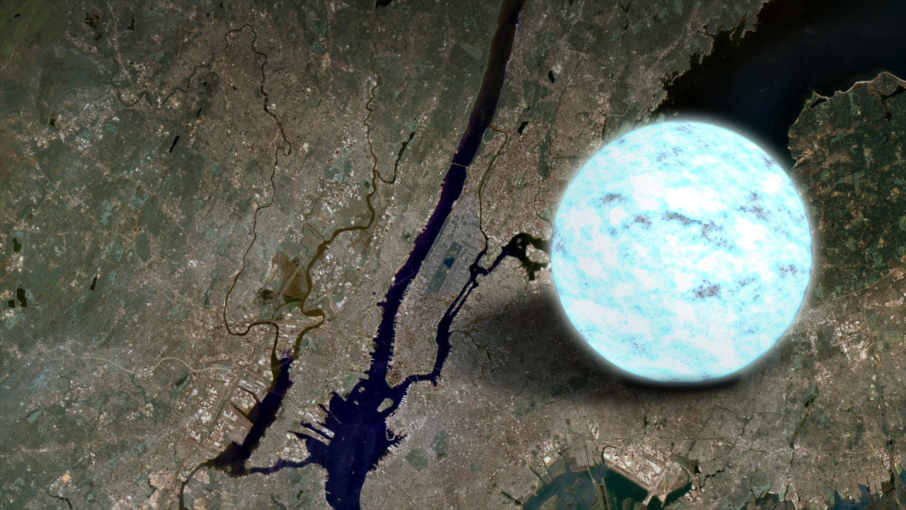 A satellite view shows the island of Manhattan and the surrounding area. The map is split by a blue river that widens toward the bottom of the image with smaller tributaries feeding into it. The landscape is in shades of brown near the river, with some small white structures visible. The landscape fades to greens toward the edges. To the right of Manhattan is an illustration of a neutron star. The glowing orb is mottled with shades of pale and electric blue. The neutron star is roughly as wide as Manhattan is long. 