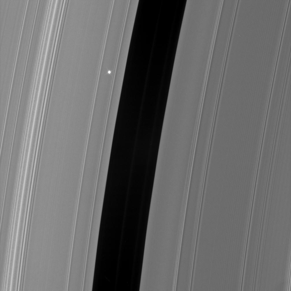 The rings of Saturn appear as wide gray blocks that take up nearly the entire image. They are streaked with lines of lighter and darker gray that run nearly vertically, tipped just a bit to the right. There’s a wide gap of black running up the middle of the image. Just to the left of center, embedded in the gray of the rings, there is a small bright spot that is Aldebaran. 