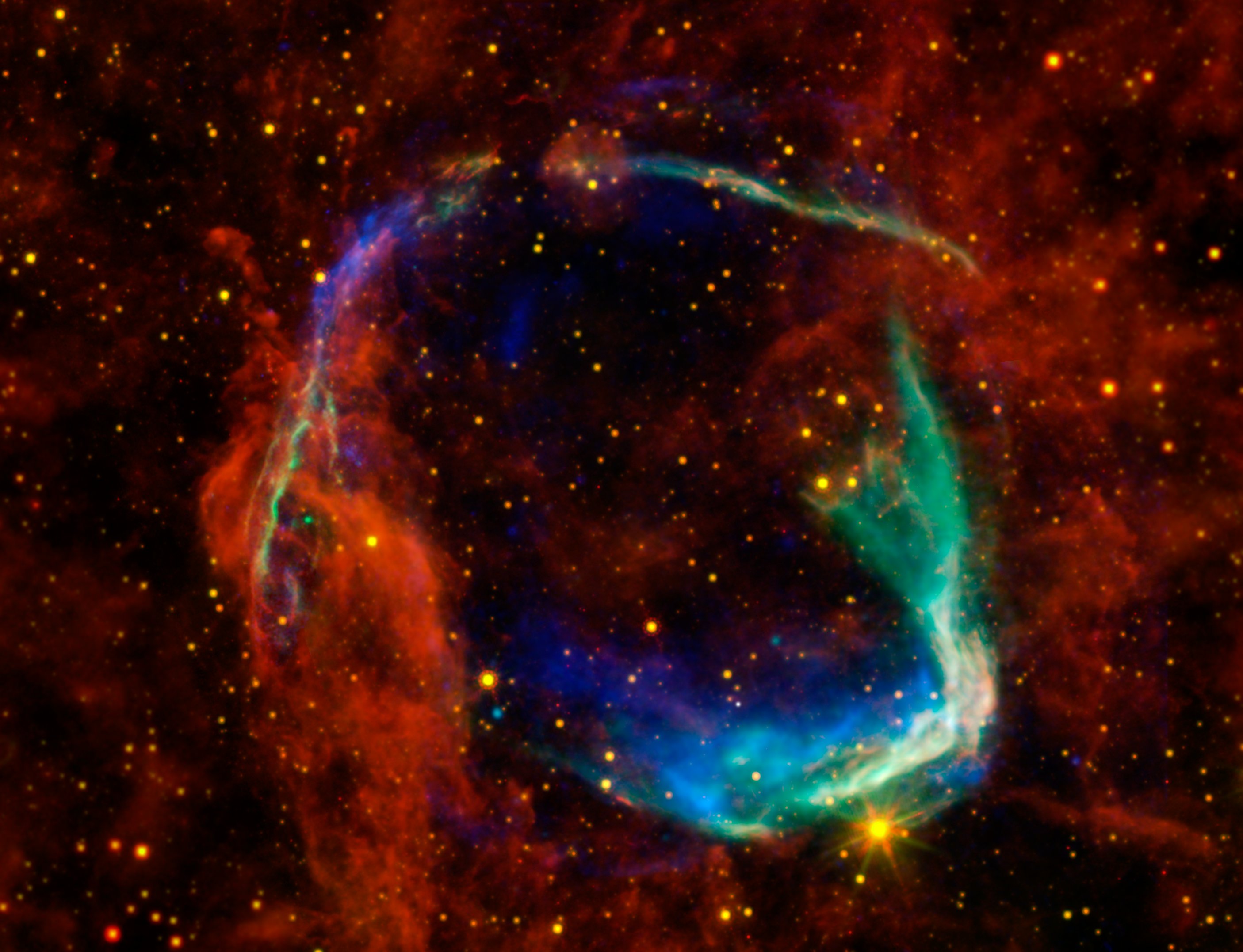 This starry background has red clouds scattered across the image. There’s a wide arc of blue, white and green at the bottom right of the image, and a thin arc running over the left and top of the image. Together these arcs almost form a circle.